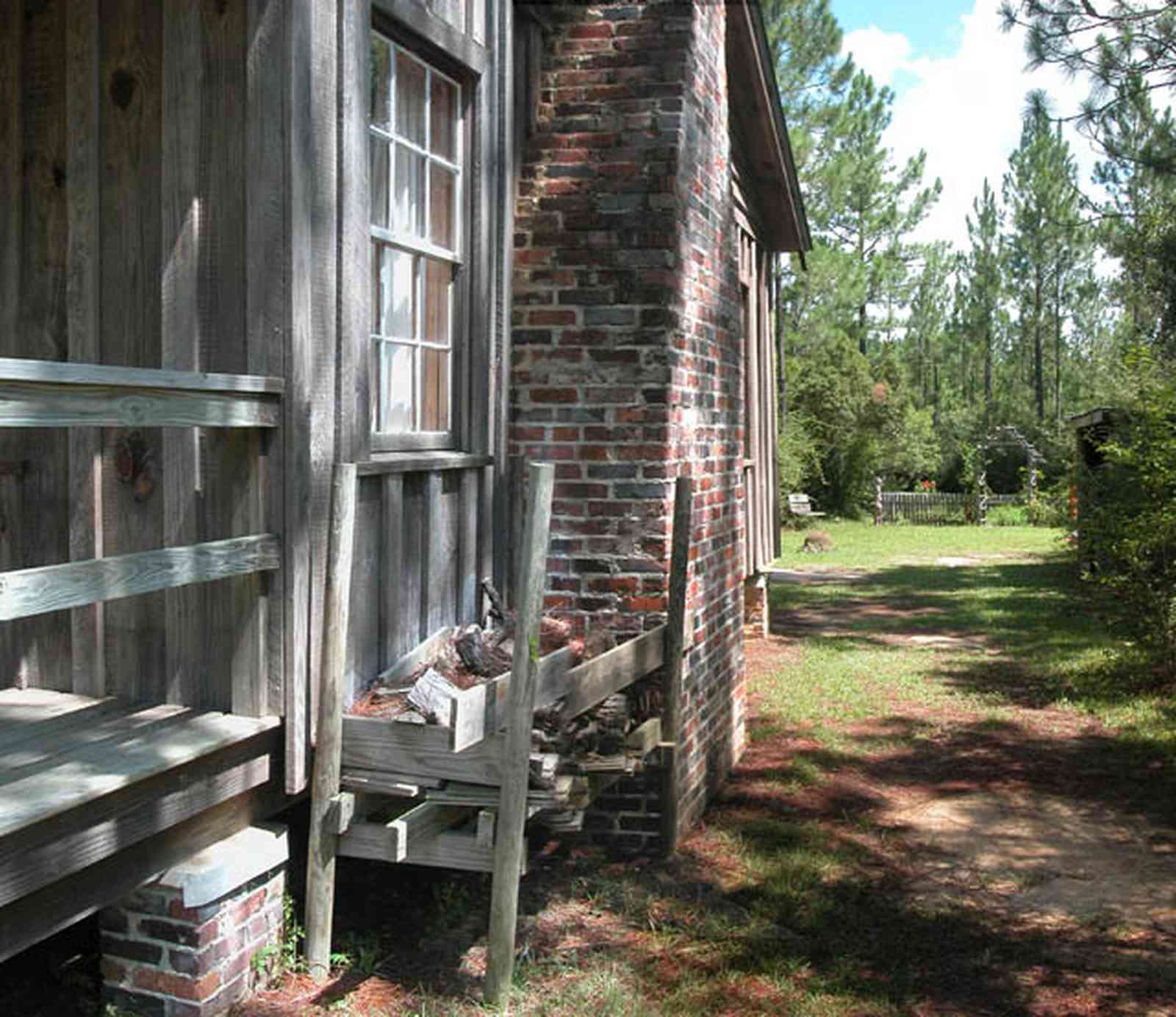 Cantonment:-Roy-Hyatt-Environmental-Center-Dog-Trot-House_07.jpg:  dog trot house, wisteria vine, porch, pine tree, board and batten, wood pile, brick piers