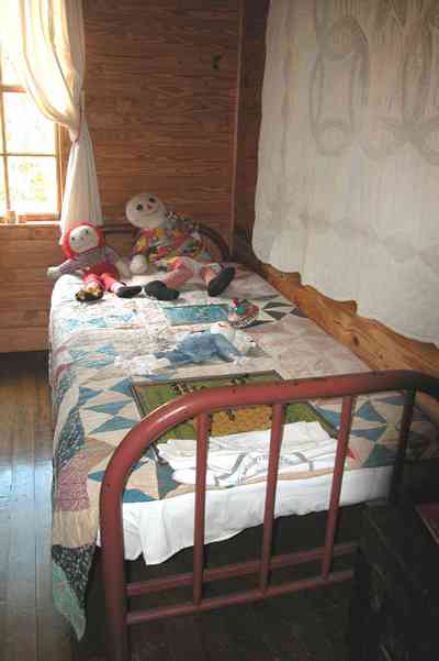 Cantonment:-Roy-Hyatt-Environmental-Center-Dog-Trot-House_10.jpg Cantonment:-Roy-Hyatt-Environmental-Center-Dog-Trot-House_10.jpg: iron bed, quilt, ragdoll, bedroom, wooden walls, wood floor, rocking chair