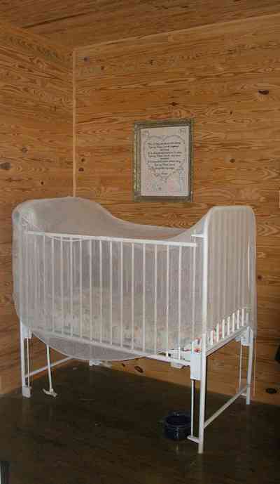 Cantonment:-Roy-Hyatt-Environmental-Center-Dog-Trot-House_14.jpg Cantonment:-Roy-Hyatt-Environmental-Center-Dog-Trot-House_14.jpg: iron bed, quilt, ragdoll, bedroom, wooden walls, wood floor, rocking chair