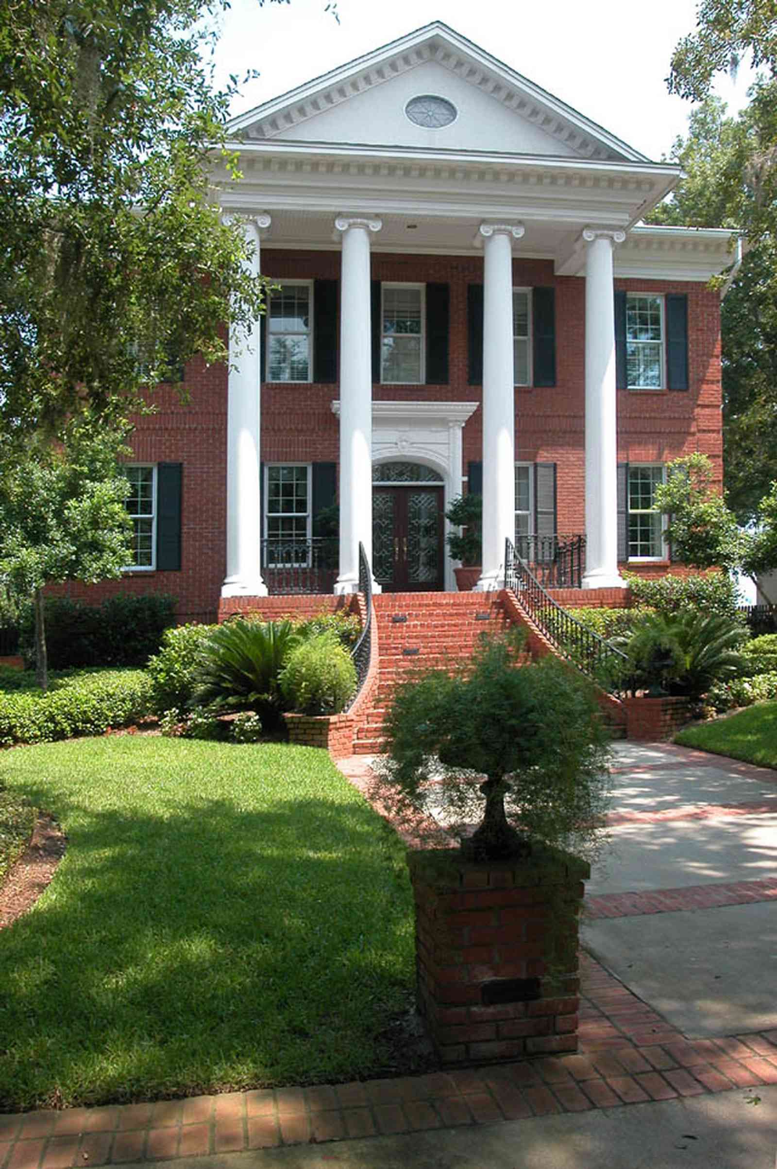 Gulf-Breeze:-506-Kenilworth-Drive_01a-copy.jpg:  red brick mansion, white columns, leaded glass door, mailbox, impatiens, brick wall, spanish moss, oak trees, fern, sidewalk, wrought-iron, doric columns, shutters, porch
