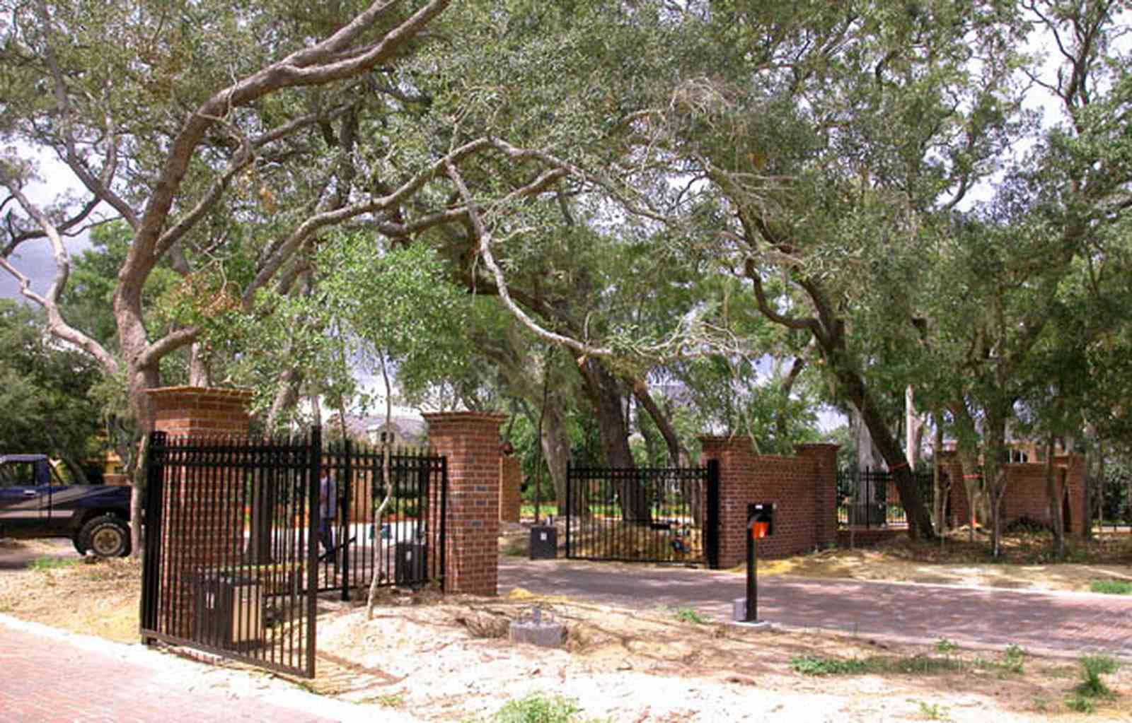 Gulf-Breeze:-706-Fair-Point-Drive_03.jpg:  gate, entrance, formal driveway, lanterns, oak trees, privacy gate, wrought-iron fence, brick columns