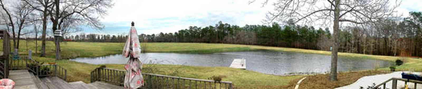 Milton:-Floyd-Farm_04.jpg:  porch, deck, fireplace, log cabin, hills, valley, pond, oak trees, sofa, chaise lounge, umbrella table, lake