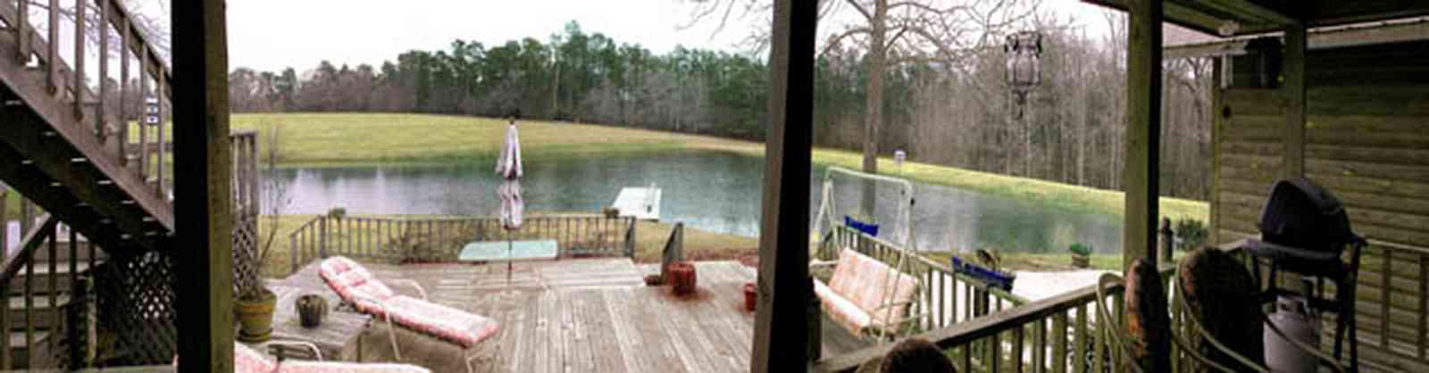 Milton:-Floyd-Farm_04a.jpg:  porch, deck, fireplace, log cabin, hills, valley, pond, oak trees, sofa, chaise lounge, umbrella table, lake