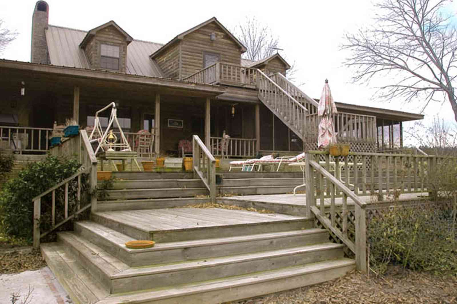 Milton:-Floyd-Farm_05.jpg:  porch, deck, fireplace, log cabin, hills, valley, pond, oak trees, sofa, chaise lounge, umbrella table, lake, 