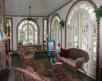 North-Hill:-105-West-Gonzales-Street_09.jpg:  leaded glass windows, wicker furniture, ceiling fan, brick fireplace, oriental rug, sunroom