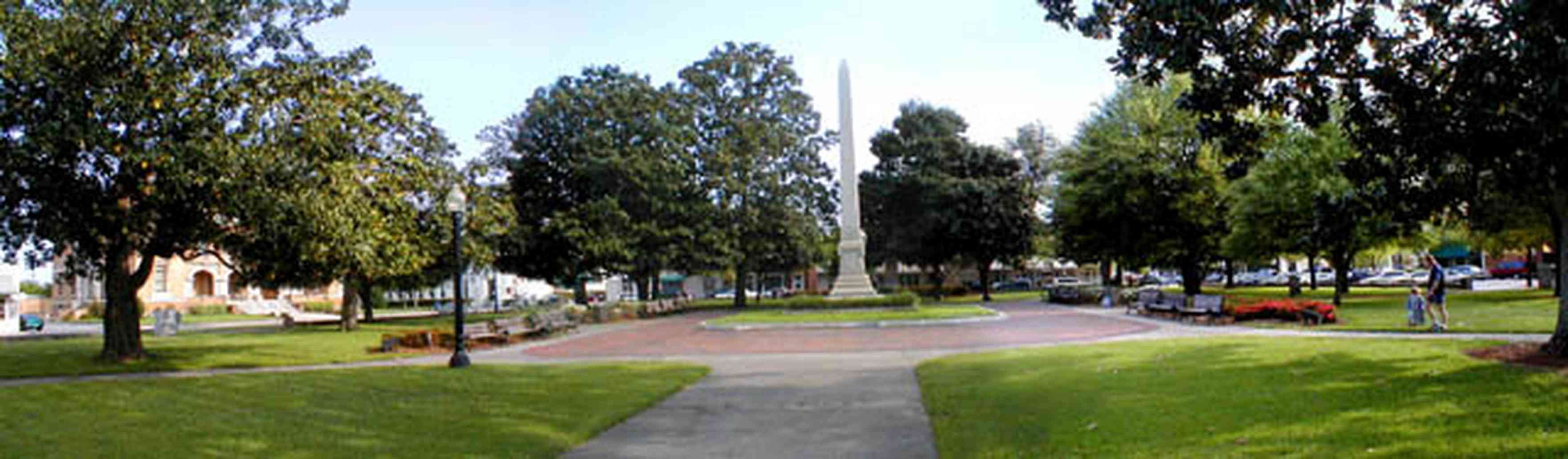 Pensacola:-Palafox-Historic-District:-Ferdinand-Plaza_00a.jpg:  stone wall, monument, oak tree, magnolia trees, spanish tile sidewalk